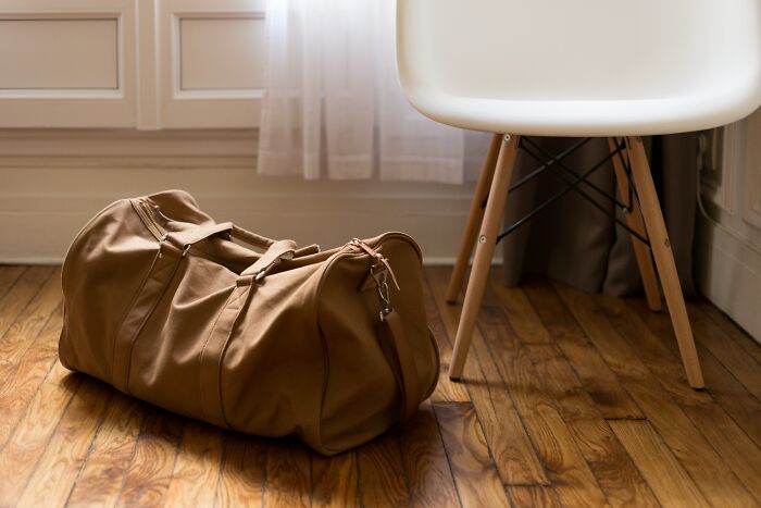 Brown travel bag resting on wooden floor next to a white chair, related to taxi and Uber drivers' stories.