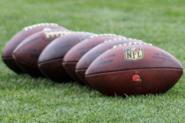 Five NFL footballs lined up on green grass, related to stories from taxi and Uber drivers about unexpected job encounters.