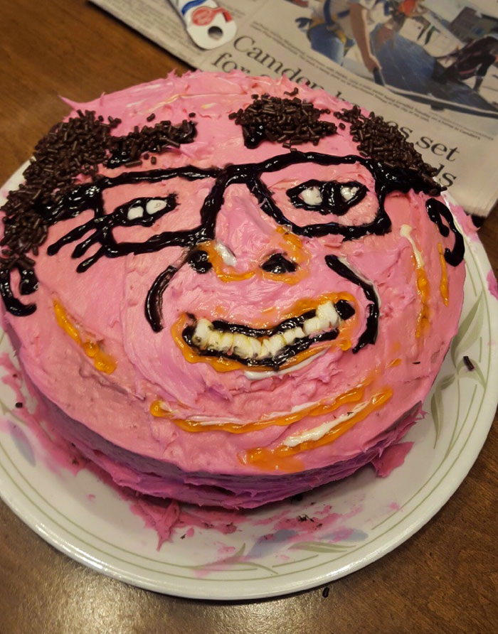 A funny cake fail with a messy chocolate face design on pink frosting.
