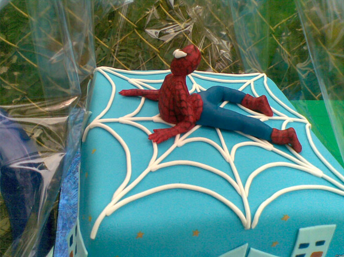 Spiderman-themed cake fail with figurine lying awkwardly on a blue web design.