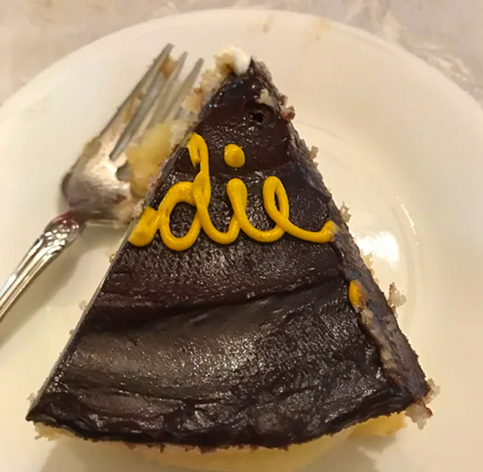 Slice of chocolate cake with "die" written in yellow icing, showcasing a humorous cake fail.