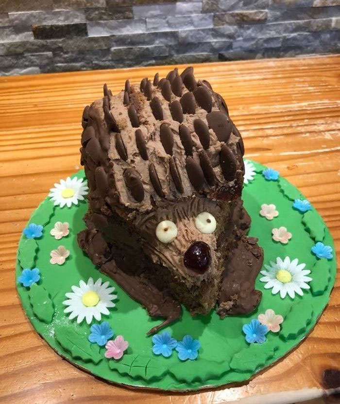 Hedgehog cake fail with chocolate spikes on a green platter decorated with colorful fondant flowers.