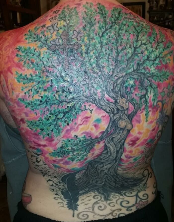 Back tattoo of a tree with colorful leaves and a background, representing a detailed design.