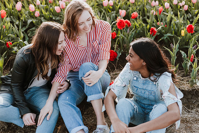 Three women sitting together in a flower garden, laughing and enjoying each other's company, highlighting things easier for women.