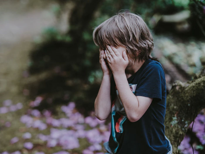 Young child covering face with hands outdoors, illustrating different perspectives on what things are easier if you're a woman.