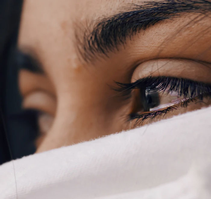 Close-up of a woman's eye with long eyelashes partially covered by white fabric, illustrating things easier if you're a woman.