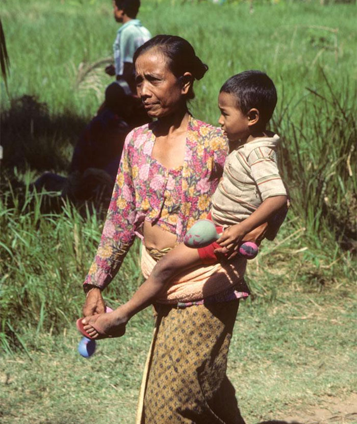 Woman carrying a child outdoors in a rural area showing daily life moments easier if you're a woman.