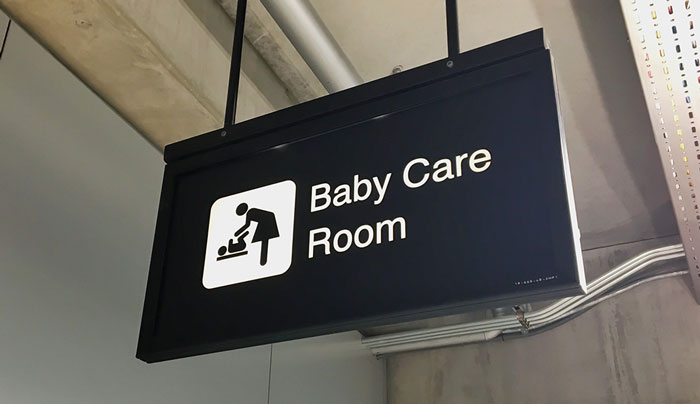 Black sign hanging from ceiling indicating baby care room with icon of woman changing baby, relating to what things are easier if you're a woman.