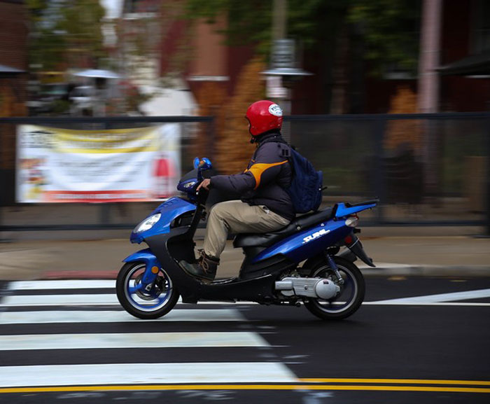 Person wearing a red helmet riding a blue scooter across a city street, symbolizing dodging a huge tactical nuke.