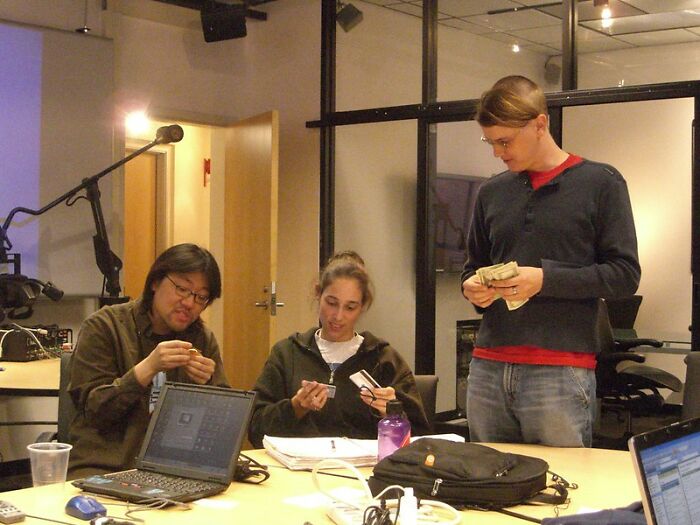 Three young adults in an online group sharing real world secrets and advice around a table with laptops and notebooks.