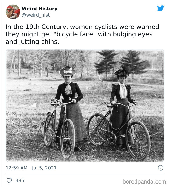 Two women in 19th century dresses and hats posing with vintage bicycles in a grassy outdoor setting, weird history fact.