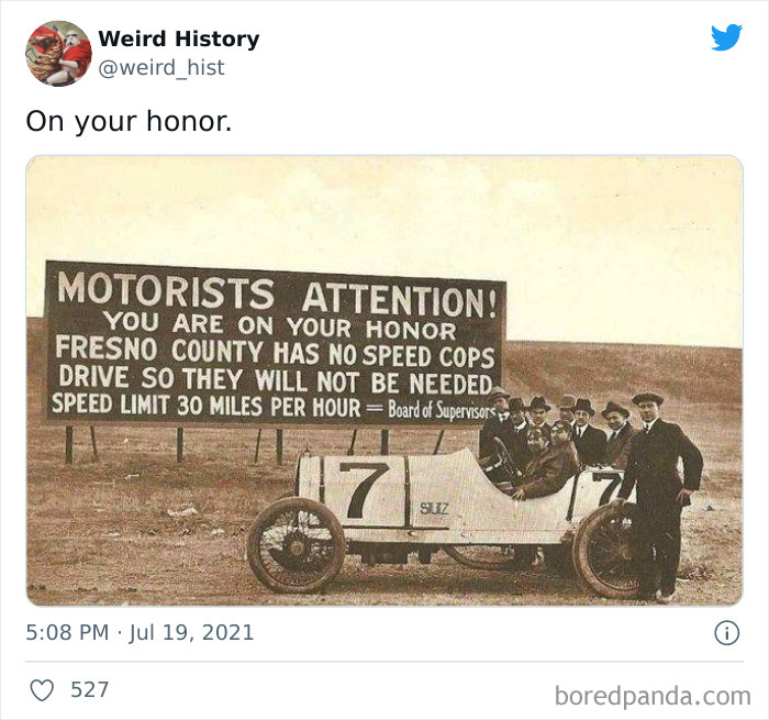 Vintage photo showing early race car and group of men near a historic roadside sign about motorists’ attention and speed limits.