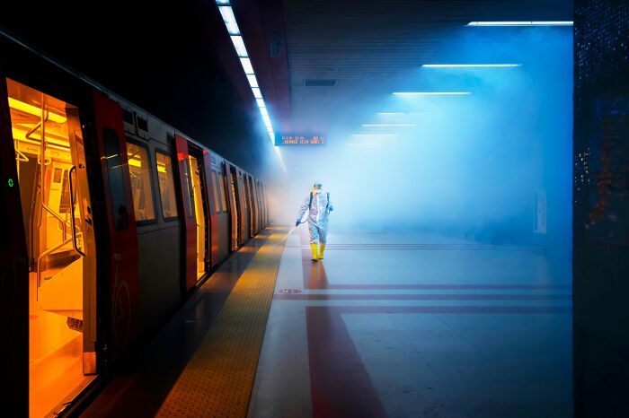 Person in protective suit walking through foggy subway platform with vivid lighting, captured in powerful Siena International Photo Awards.