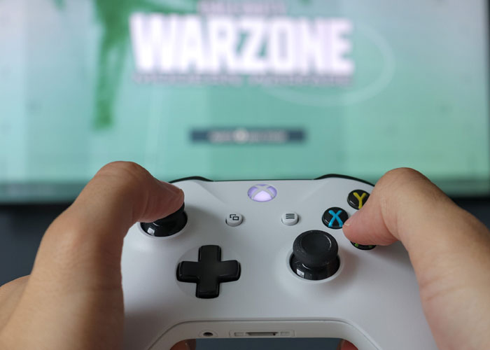 Person holding a white Xbox controller playing a video game highlighting scams in daily lives concept.