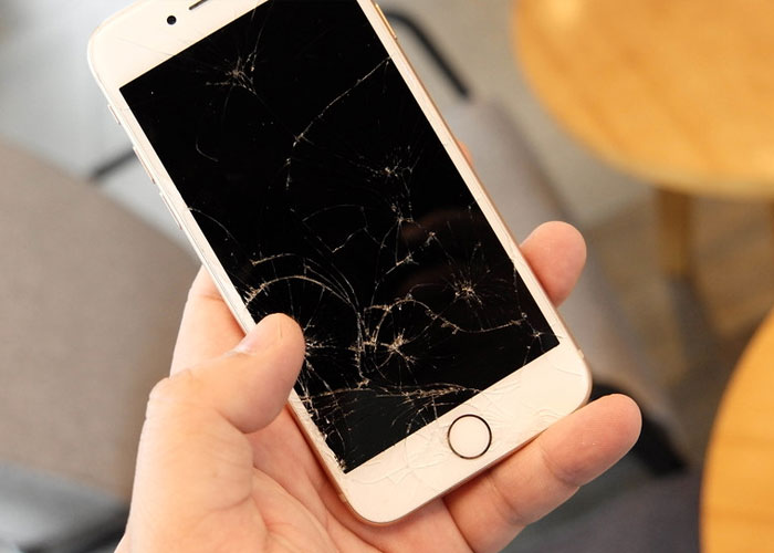 Hand holding a smartphone with a severely c*****d screen, illustrating common scams in daily lives.