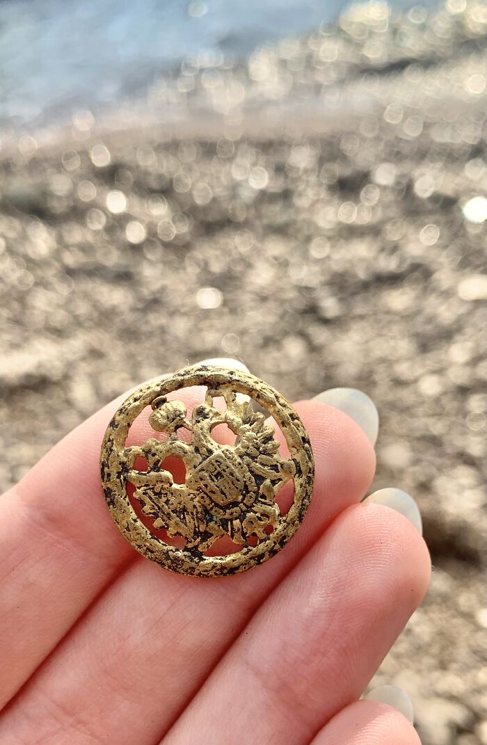 Hand holding an antique metal button found on the beach during treasure hunting for antique items washed ashore.