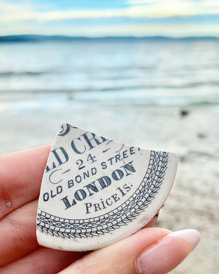 Hand holding a piece of antique pottery found washed up on the beach during a treasure search by the shore.