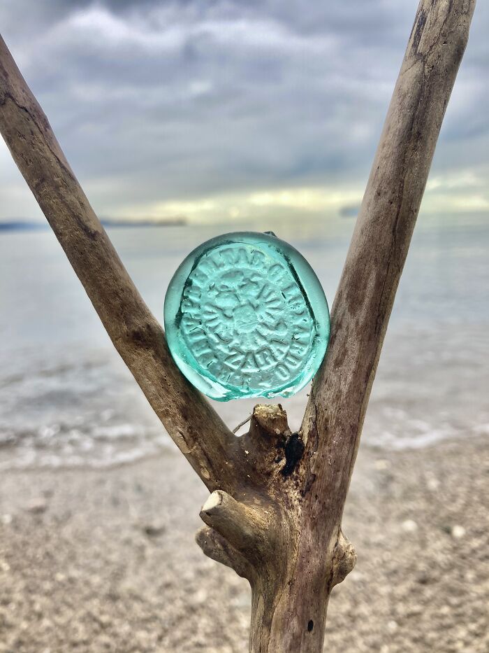Antique sea glass treasure found on the beach displayed between branches with ocean and sky in the background.
