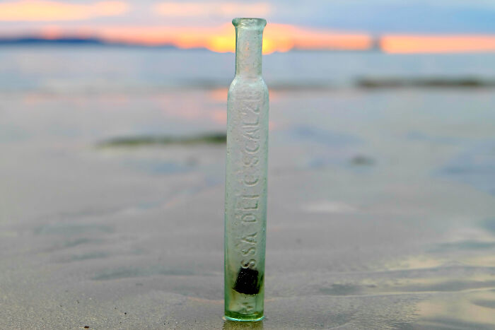 Antique glass bottle found washed up on the beach during treasure search at sunset shore.