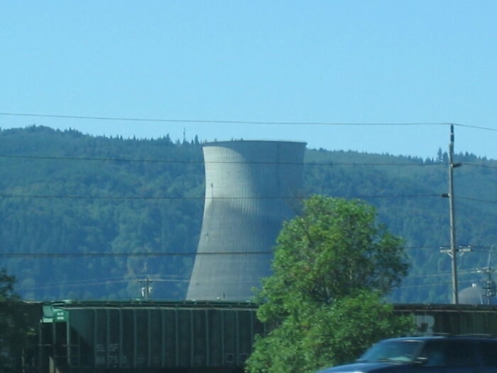 Cooling tower of a nuclear power plant with hills in the background and a car passing in the foreground.