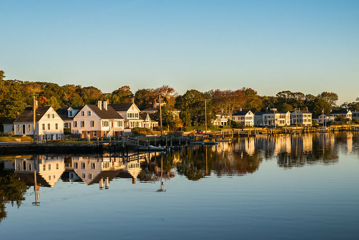 Waterfront houses reflecting in calm water during golden hour, symbolizing moments of dodging huge tactical nukes.