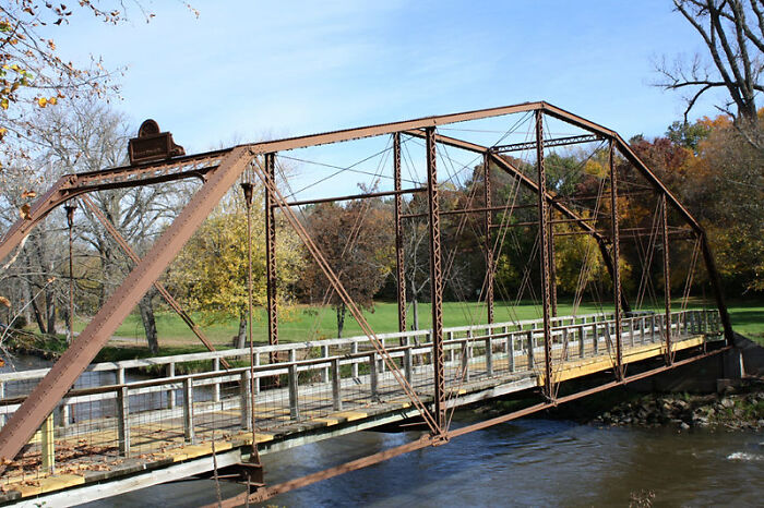Rusty iron truss bridge over a river with fall trees in the background representing tactical nuke dodged metaphor.
