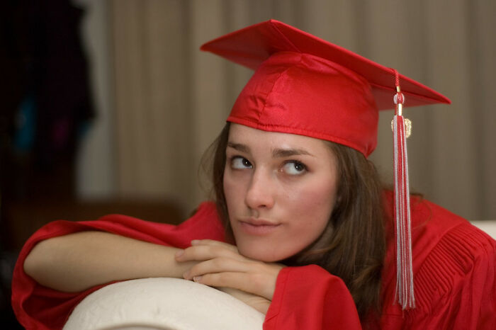 Young adult in red graduation cap and gown, reflecting on real world secrets shared in online advice group.