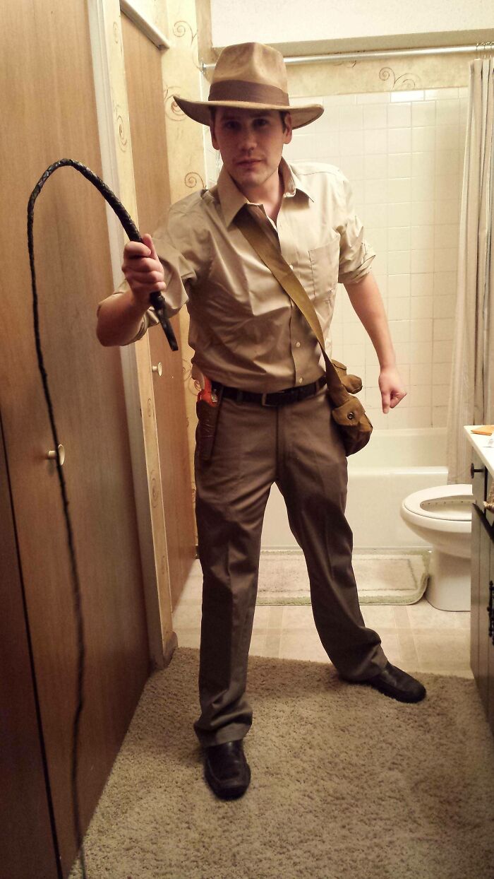 Man in a simple Indiana Jones inspired Halloween costume with hat, whip, and satchel in a bathroom setting