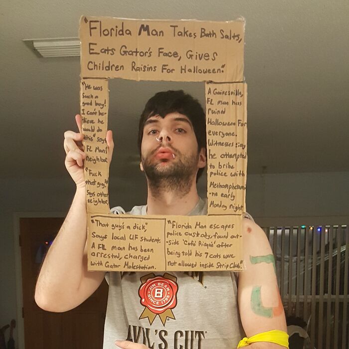 Man wearing a simple Halloween costume made from cardboard with handwritten text, showing creative effort and humor.