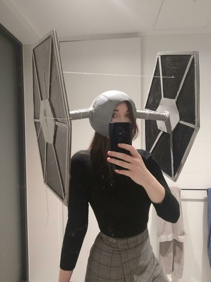 Person wearing a creative Halloween costume with large homemade starfighter wings made from cardboard and tape.