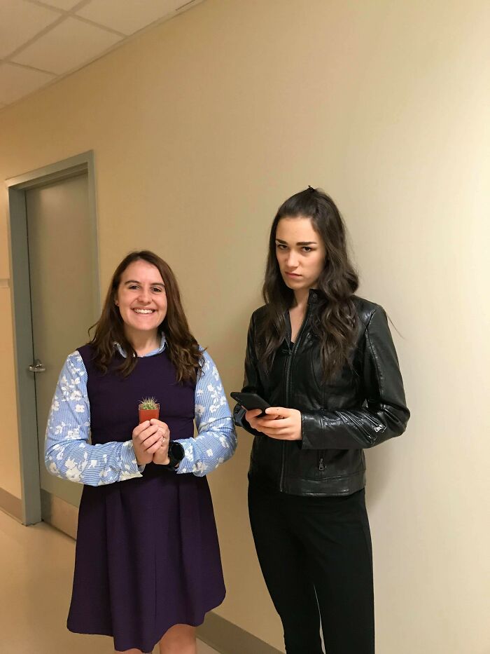 Two women in simple Halloween costumes, one holding a small cactus and the other wearing a black leather jacket.