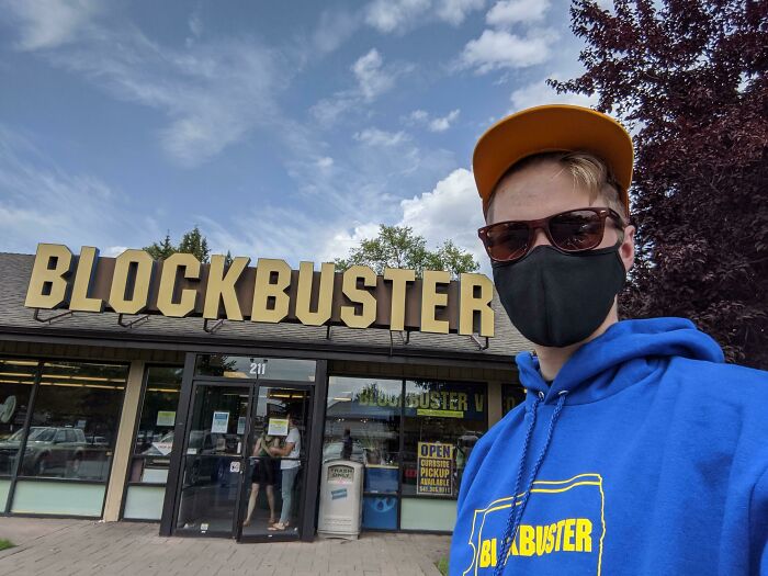 Person in Blockbuster attire outside a store, highlighting nostalgic 2000s culture.