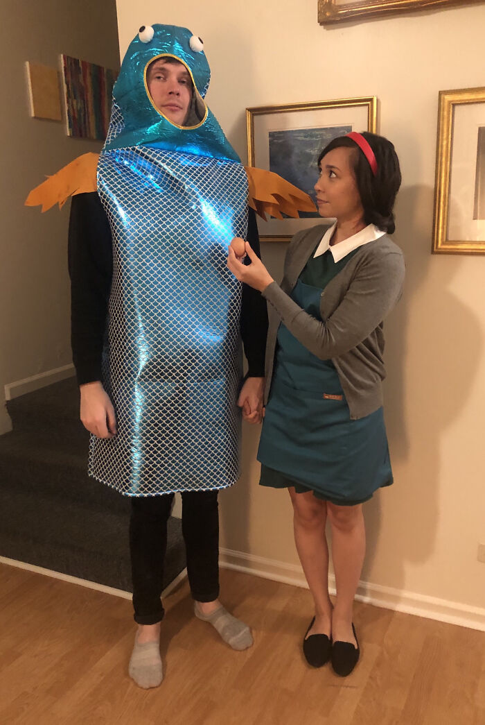 Man dressed in a simple fish costume and woman in a dress acting out a playful scene for Halloween costumes.