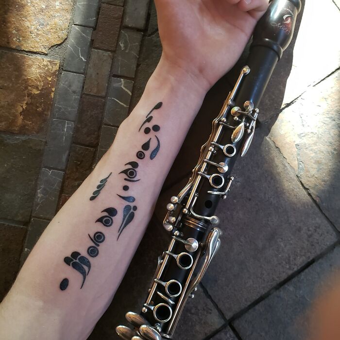 Tattoo of abstract musical notes on an arm beside a clarinet, showcasing an interesting first tattoo idea.