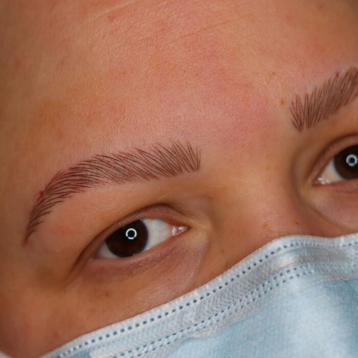 Close-up of a person's eyes showing detailed eyebrow tattoos while wearing a blue surgical mask.