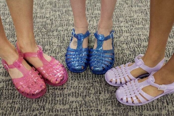 Colorful jelly sandals from the 2000s in pink, blue, and purple worn on a carpeted floor.