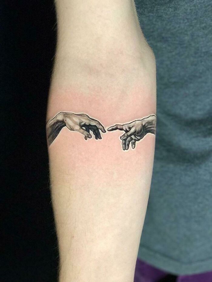 Tattoo of two hands reaching towards each other on a person's forearm, inspired by intricate first tattoo ideas.