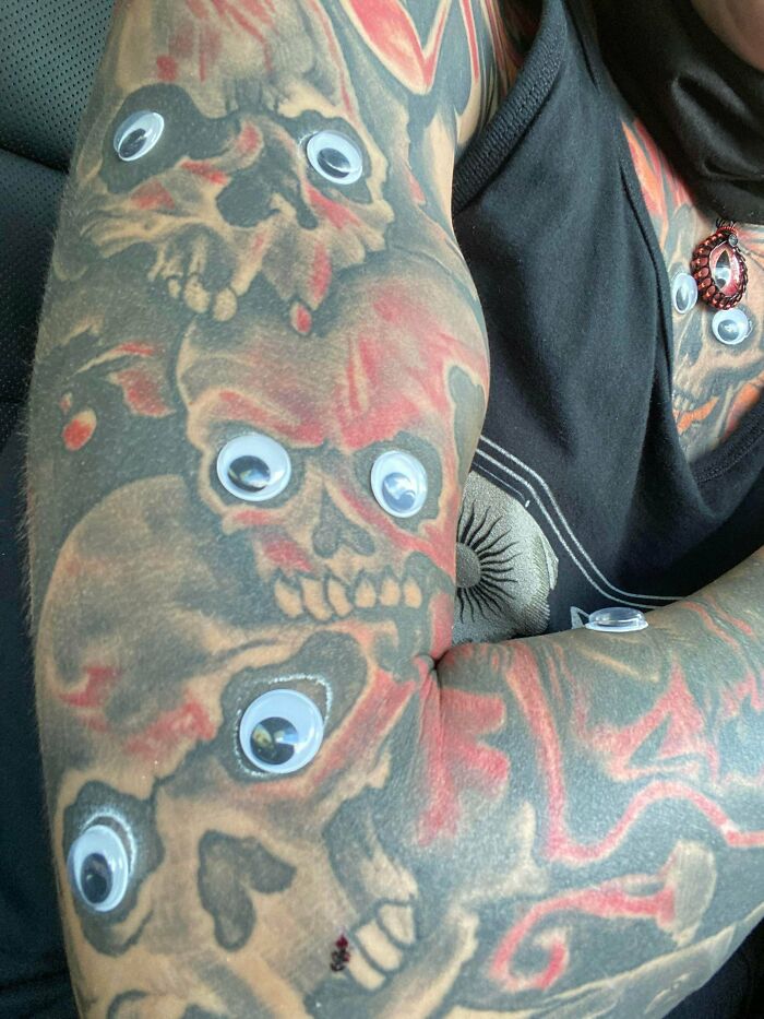 Spooky Halloween tattoo with skulls and googly eyes on an arm, showing vibrant red and black ink design.