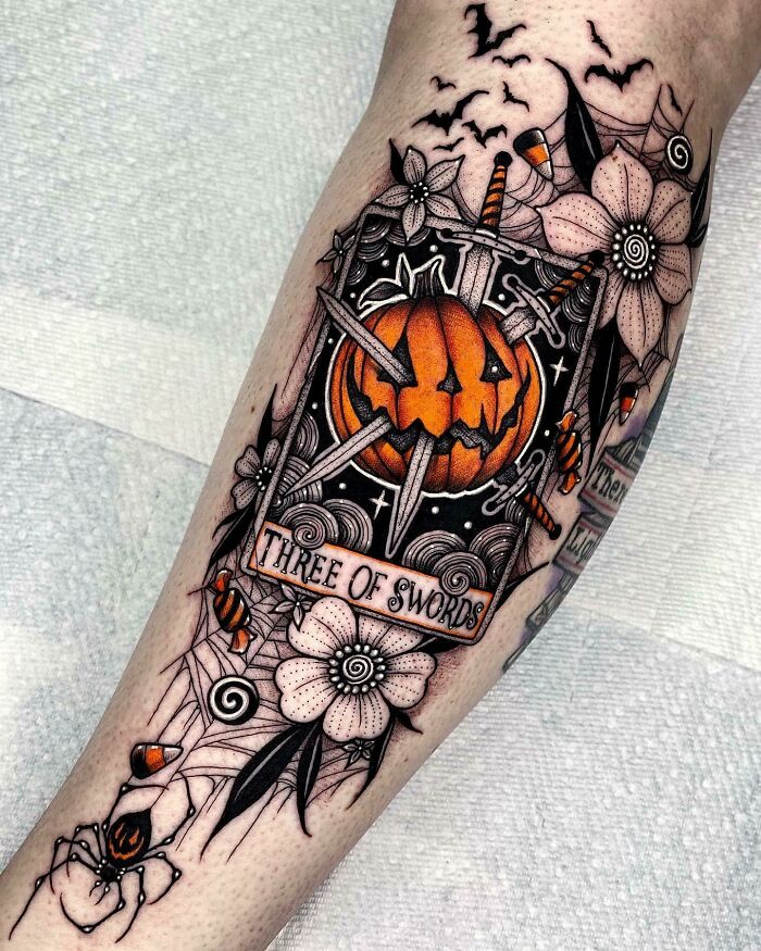 Spooky Halloween tattoo featuring a jack-o'-lantern with swords and floral elements on a person's leg.