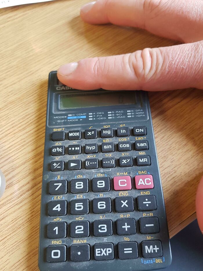 Vintage 2000s calculator with buttons and display, a finger pressing a key, on a wooden desk.