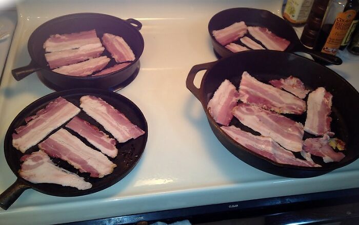 Four cast iron skillets on a stove cooking thick bacon strips, symbolizing real world secrets shared in an online group.