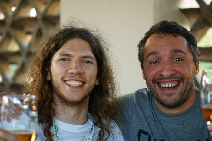 Two young men smiling and holding drinks, sharing advice about the real world in an online group for young adults.