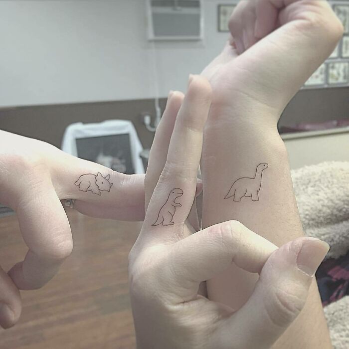 Small dinosaur tattoos on fingers and wrists, showcasing interesting first tattoo ideas.