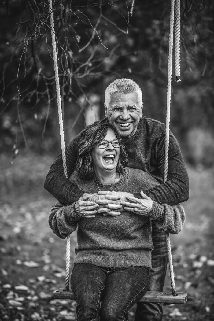 Happy older couple in love sharing a joyful moment on a swing outdoors, captured in black and white photography.