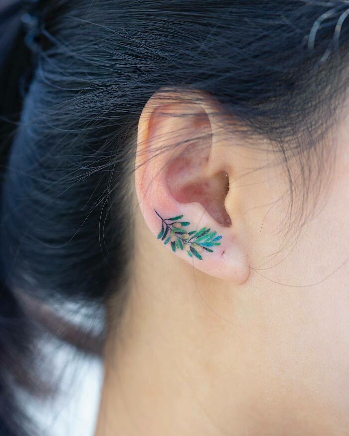 Close-up of a delicate leaf tattoo behind an ear, showcasing an interesting first tattoo idea.
