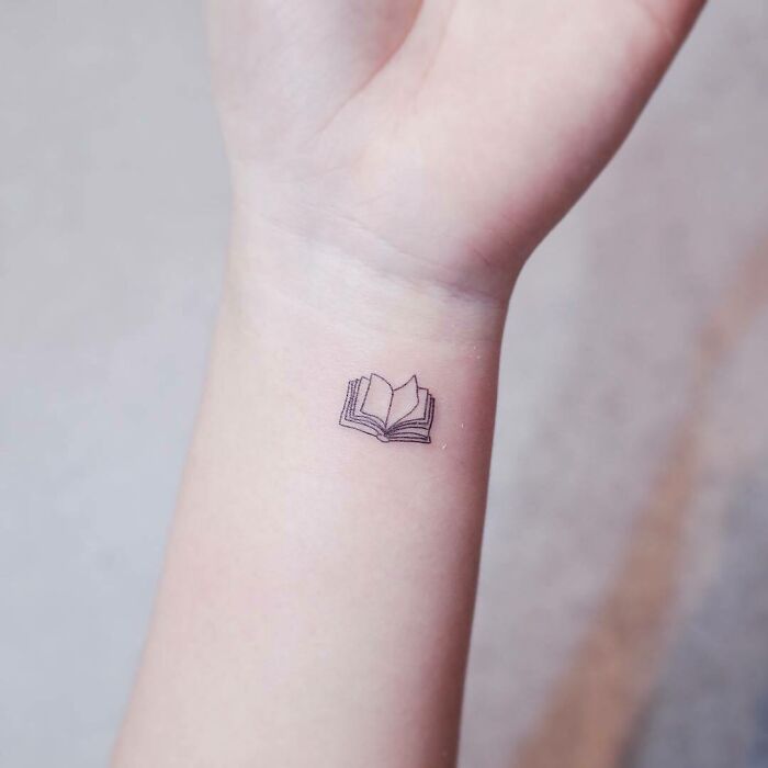Minimalist tattoo of an open book on a wrist, showcasing a simple yet interesting first tattoo idea.