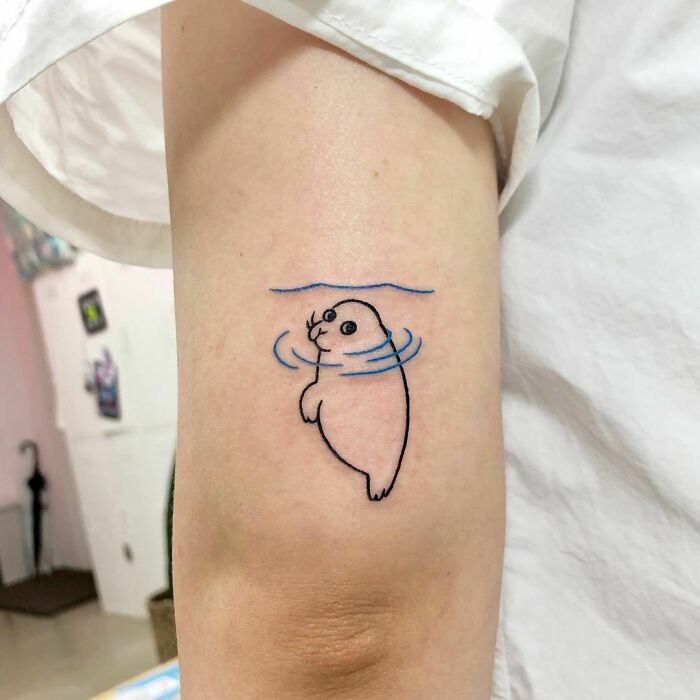 Seal tattoo on arm, showcasing an interesting first tattoo idea with simple lines and blue water accents.