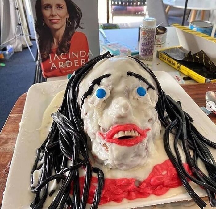 Funny cake fail resembling a person with black icing for hair and blue candy eyes on a platter.