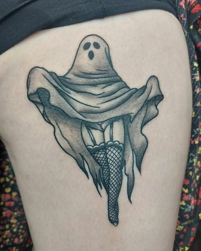 Spooky Halloween tattoo of a ghost draped in fabric with fishnet stockings on leg.