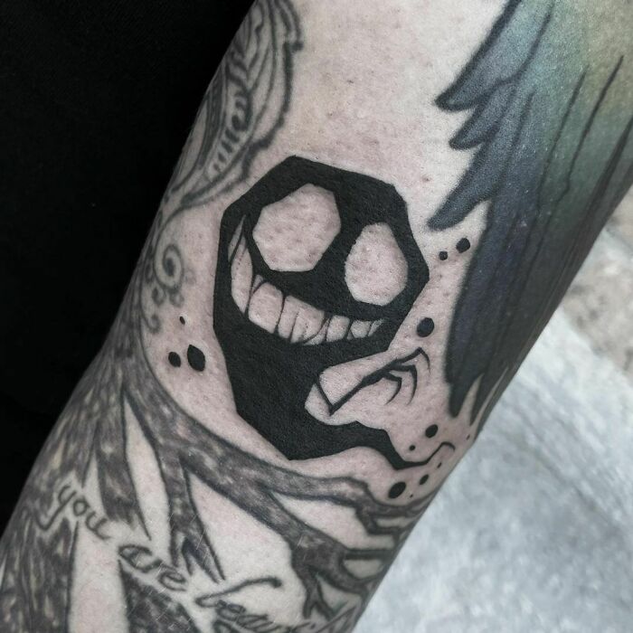 Person with a spooky Halloween tattoo featuring a grinning black ink ghost.